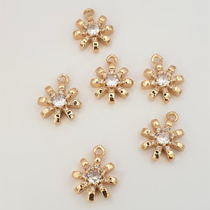 May include: Six gold-tone metal charms shaped like a starburst with a clear rhinestone in the center. Each charm has a loop at the top for attaching to a necklace or bracelet.