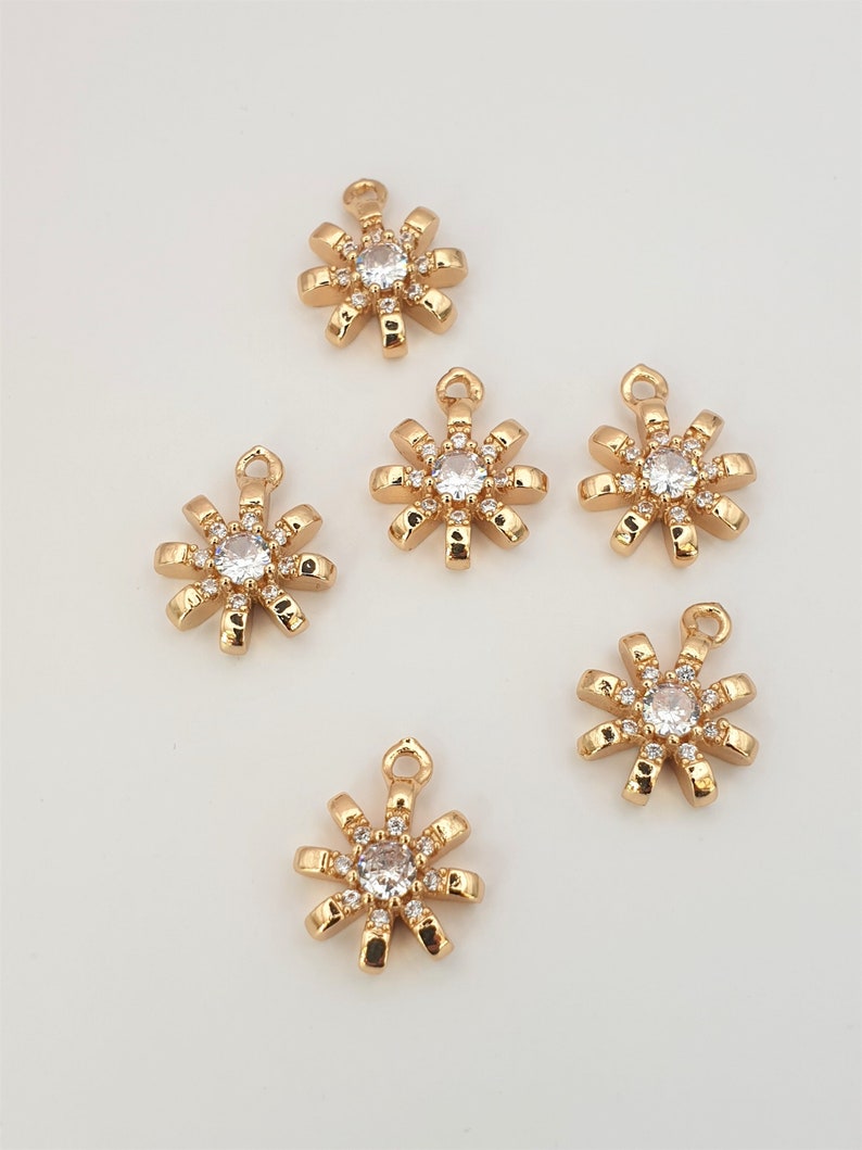 May include: Six gold-tone metal charms shaped like a starburst with a clear rhinestone in the center. Each charm has a loop at the top for attaching to a necklace or bracelet.