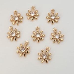 May include: Eight gold-toned metal charms shaped like a sun with a clear rhinestone in the center and smaller rhinestones around the edge.