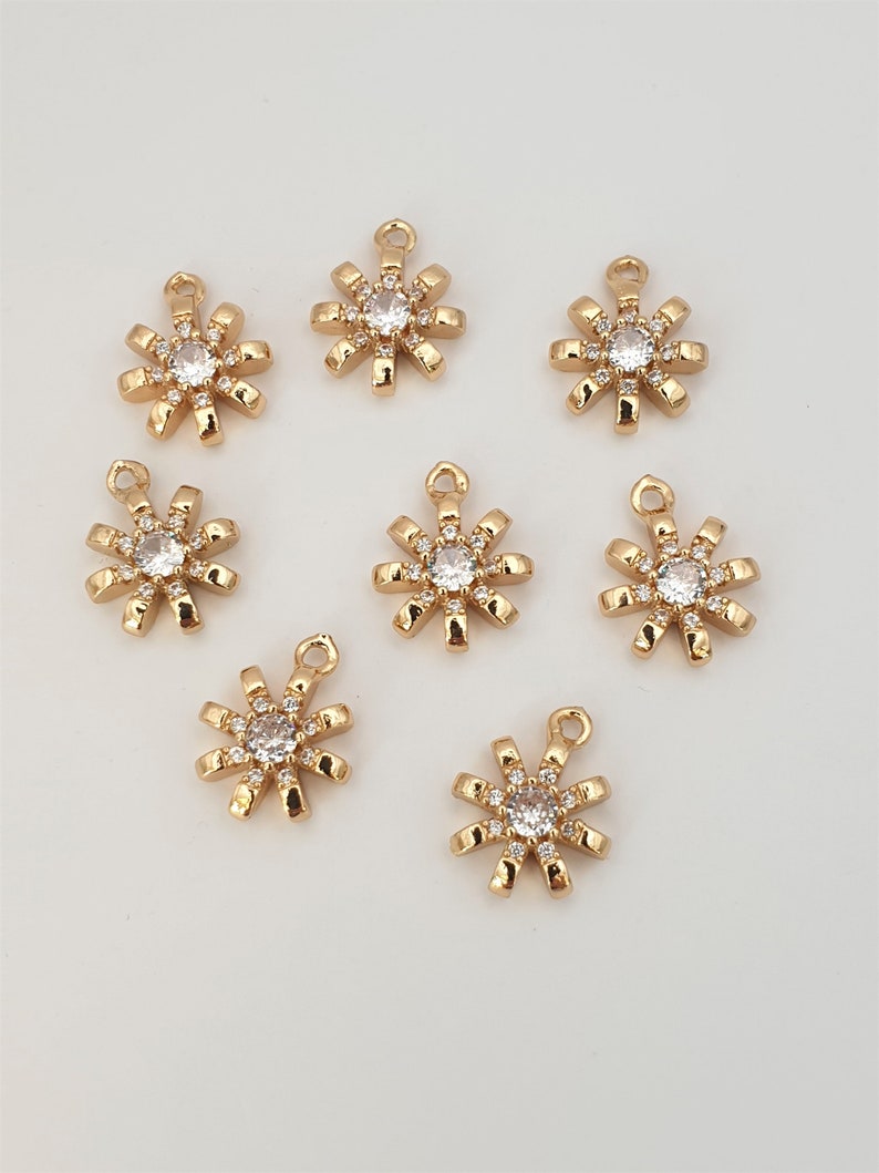 May include: Eight gold-toned metal charms shaped like a sun with a clear rhinestone in the center and smaller rhinestones around the edge.