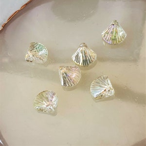 May include: Six iridescent glass seashells in various sizes and shapes. The shells are a light gold color with a rainbow iridescent sheen.