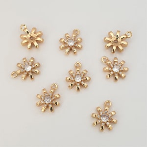 May include: Eight gold-tone metal charms in the shape of a sunburst with a clear rhinestone in the center. Each charm has a loop at the top for attaching to a necklace, bracelet, or other jewelry.