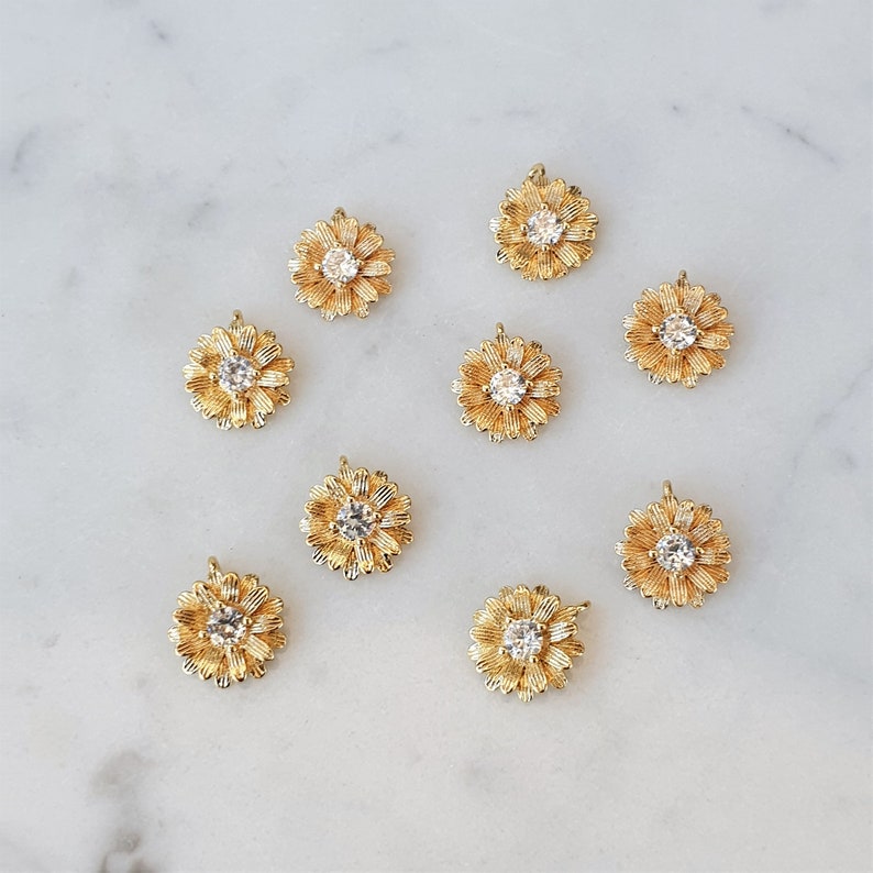 May include: Ten gold-tone flower charms with clear rhinestone centers. The charms are perfect for jewelry making or adding a touch of sparkle to crafts.