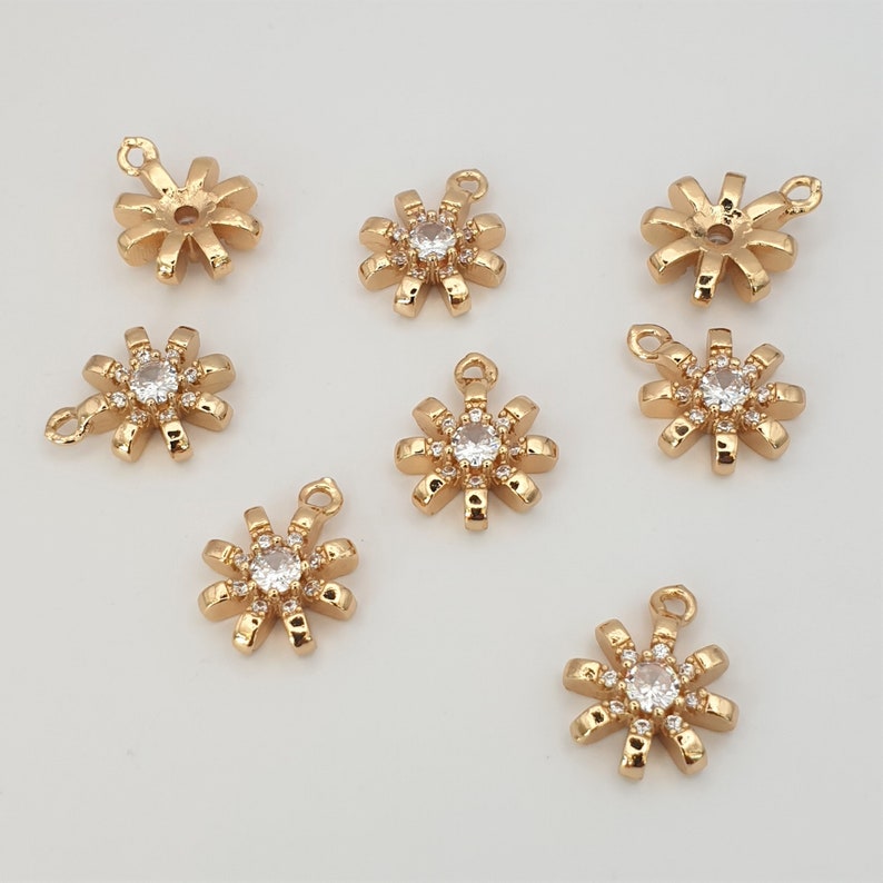May include: Eight gold-tone metal charms in the shape of a starburst with a clear rhinestone in the center. The charms have a loop at the top for attaching to jewelry.