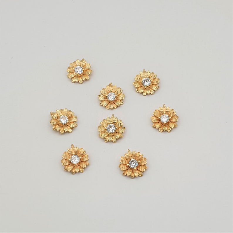 May include: Eight gold-tone flower charms with clear rhinestone centers. The charms have a loop on the back for attaching to jewelry or other crafts.