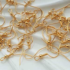 May include: A pile of gold-toned earring hooks with a spring-loaded closure. The hooks are made of metal and have a small ball at the top.