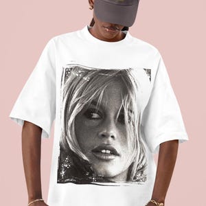 Op de afbeelding: Wit T-shirt met een zwart-wit portret van een vrouw. De afbeelding heeft een verweerde rand. Het shirt heeft korte mouwen en een ronde hals.