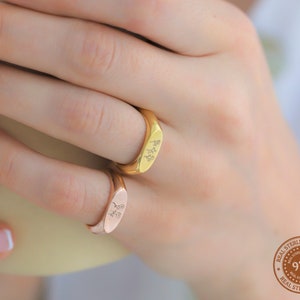 May include: Two gold and rose gold signet rings with a floral design. The rings are worn on a finger. The image also includes a round sticker with the text "Real Sterling Silver 925 Real Sterling Silver".