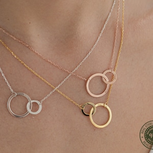 May include: Three silver necklaces with interlocking circle pendants. The necklaces are layered on a model's neck. The pendant on the bottom necklace is silver, the middle necklace is rose gold, and the top necklace is gold. The pendant on the top necklace has the words "Mom" and "Dad" engraved on it.