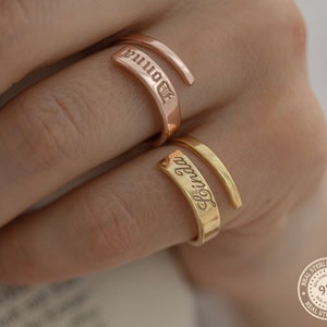 May include: Two gold rings with the words "Donna" and "Olivia" engraved on them. The rings are worn on a person's fingers.