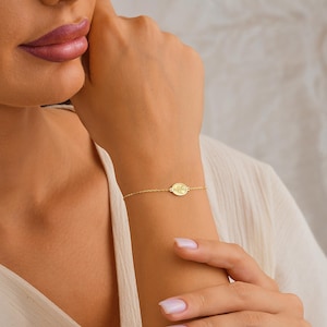 May include: A gold chain bracelet with a small oval charm. The charm has a delicate floral design.