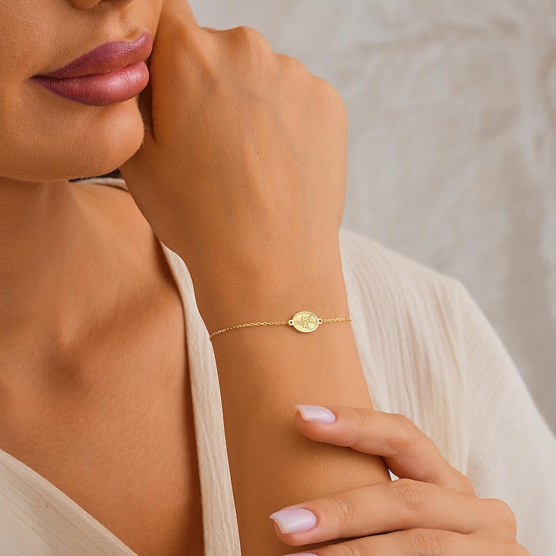 May include: A gold chain bracelet with a small oval charm. The charm has a delicate floral design.