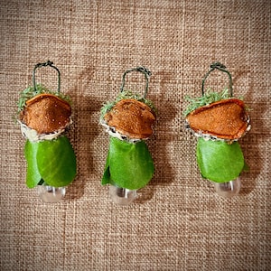 May include: Three hanging ornaments featuring a brown dried citrus slice top, a layer of green moss, a green fabric leaf skirt, and a clear glass bead base. Each ornament is suspended by a thin dark green wire loop attached to the top of the citrus.