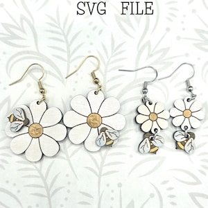 Puede incluir: Pendientes de margarita blancos con centros dorados y pequeños detalles de abeja. Los pendientes están cortados con láser y presentan un diseño floral. La imagen incluye el texto "Glowforge Ready" y "SVG FILE". También se incluye el texto "not a physical product".