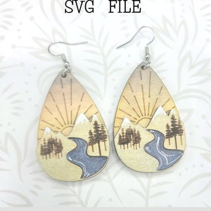 May include: A pair of wooden earrings with a sunrise mountain scene and a river. The earrings are teardrop shaped and have silver hooks. The earrings are a digital download, not a physical product. SVG FILE.