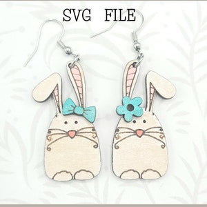 May include: A pair of laser-cut wooden bunny earrings with blue and pink accents. The earrings are ready to be made with a Glowforge. SVG FILE.