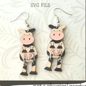 Könnte beinhalten: Ein Paar Kuh-Ohrringe mit schwarzen und weißen Flecken, rosa Nasen und braunen Beinen. Die Ohrringe sind aus Holz und haben silberne Haken. Das Bild enthält den Text "Glowforge Ready SVG FILE" und "not a physical product".
