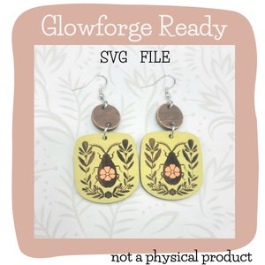 May include: A pair of wooden earrings with a light green background and a black bug design. The bug has a pink flower on its back. The earrings are attached to silver hooks and have a brown wooden circle at the top.