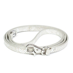 May include: Silver-colored dog leash with a snakeskin pattern. The leash is made of a flexible material and features a silver metal clasp and a loop for the handle. The leash is coiled on a white background.