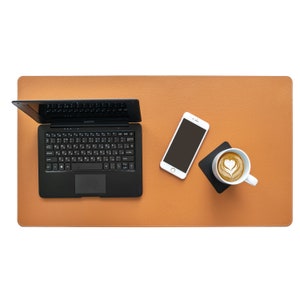 Könnte beinhalten: Eine braune Leder-Schreibtischunterlage mit einem Laptop, einem weißen Smartphone und einer weißen Kaffeetasse mit Latte-Art auf einem weißen Untersetzer.