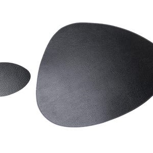 Puede incluir: Dos manteles individuales negros con superficie texturizada. Uno es un óvalo grande de forma irregular, y el otro es más pequeño y de forma similar. Los manteles individuales están hechos de un material que se asemeja al cuero.