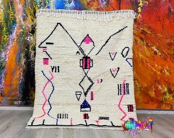 Peut inclure: Tapis marocain blanc avec un motif géométrique en noir, rose et bleu. Le tapis a une bordure à franges.