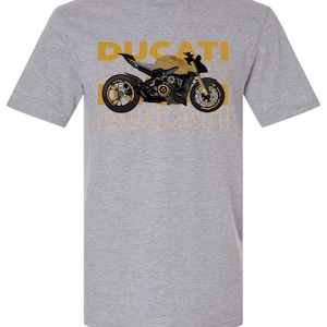 May include: A heather grey t-shirt with a black and gold illustration of a Ducati motorcycle. The word "DUCATI" is repeated three times in a yellow outline.