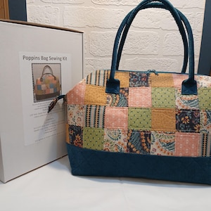 May include: A patchwork fabric bag sewing kit with a teal zipper and handles. The kit includes instructions and fabric pieces to create a bag with a patchwork design. The bag is 12 inches wide and 12 inches tall. The kit is called "Poppins Bag Sewing Kit".