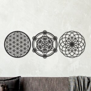 May include: Three black metal wall decor pieces featuring geometric designs. The designs are a flower of life, a metatron's cube, and a seed of life.