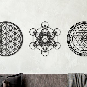 May include: Three black metal wall decor pieces featuring geometric designs. The designs are a flower of life, a metatron's cube, and a sri yantra.