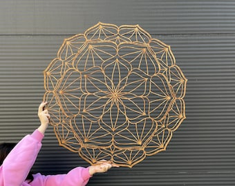 May include: A large, intricate wooden mandala with a brown finish. The mandala is circular and has a geometric design with many layers of overlapping shapes.
