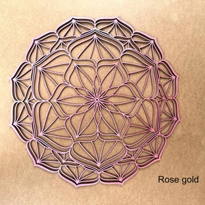 Op de afbeelding: Een roosgoudkleurige mandala wanddecoratie met een ingewikkeld geometrisch ontwerp. De mandala is gemaakt van hout en heeft een delicate, kant-achtige uitstraling.