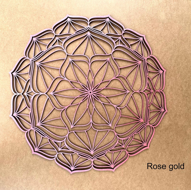 Op de afbeelding: Een roosgoudkleurige mandala wanddecoratie met een ingewikkeld geometrisch ontwerp. De mandala is gemaakt van hout en heeft een delicate, kant-achtige uitstraling.