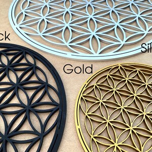 May include: Three wooden wall decor pieces in the shape of a flower of life pattern. The pieces are in black, silver, and gold.