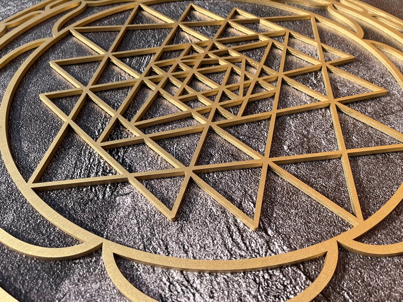 May include: A gold geometric design with a circular frame on a dark gray background. The design is made up of overlapping triangles.