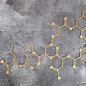 K&ouml;nnte beinhalten: Eine goldfarbene Molek&uuml;lstruktur aus verbundenen Kreisen und Linien auf einem grauen, strukturierten Hintergrund.