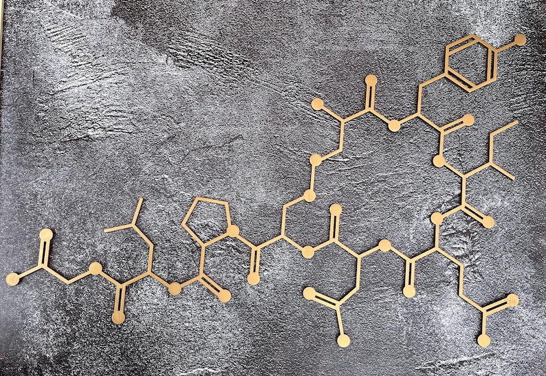 K&ouml;nnte beinhalten: Eine goldfarbene Molek&uuml;lstruktur aus verbundenen Kreisen und Linien auf einem grauen, strukturierten Hintergrund.