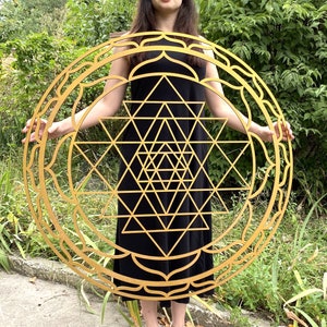 May include: A large, golden, wooden mandala with a geometric design. The mandala is a Sri Yantra, a sacred symbol in Hinduism.