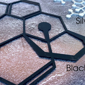 K&ouml;nnte beinhalten: Schwarze und silberne geometrische Formen, die einem Wabenmuster &auml;hneln, werden auf einem strukturierten silbernen Hintergrund angezeigt. Der Text "Black" und "Silver" ist unter den Formen sichtbar.