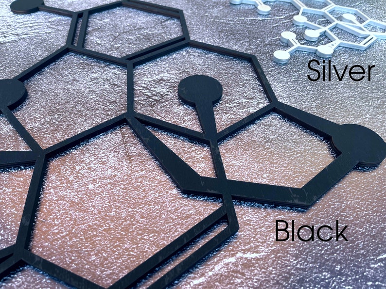 K&ouml;nnte beinhalten: Schwarze und silberne geometrische Formen, die einem Wabenmuster &auml;hneln, werden auf einem strukturierten silbernen Hintergrund angezeigt. Der Text "Black" und "Silver" ist unter den Formen sichtbar.