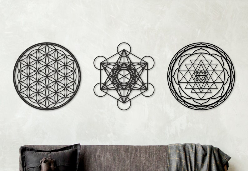 May include: Three black metal wall decor pieces featuring geometric designs. The designs are a flower of life, a metatron's cube, and a sri yantra.