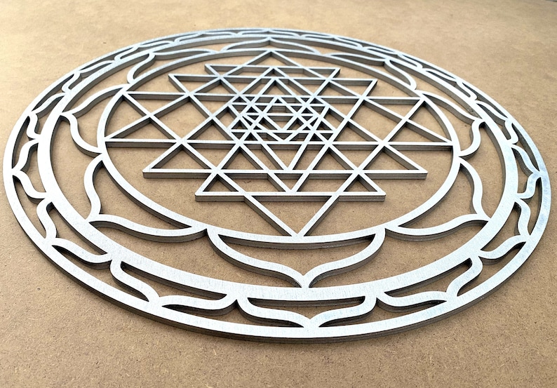 May include: A silver metal Sri Yantra mandala with a detailed geometric design. The mandala is circular and has a decorative border.