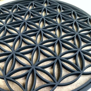 May include: A black wooden round wall decor with a geometric pattern of overlapping circles and flower shapes. The design is known as the Flower of Life.