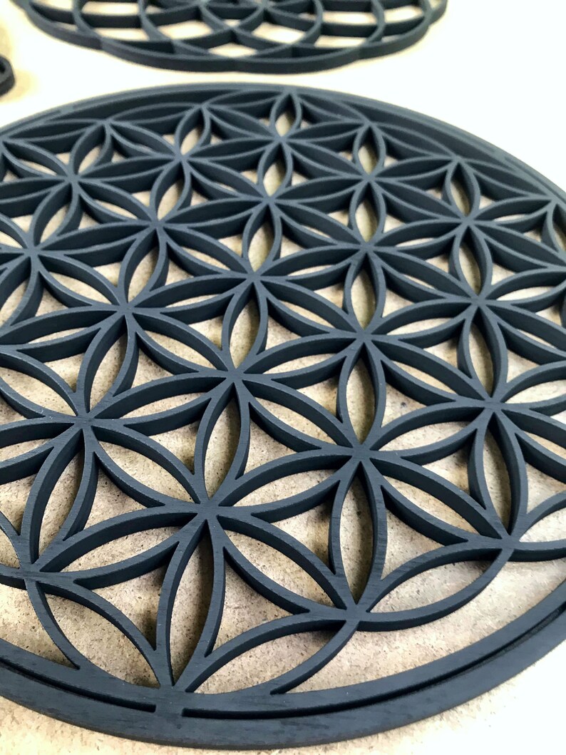 May include: A black wooden round wall decor with a geometric pattern of overlapping circles and flower shapes. The design is known as the Flower of Life.