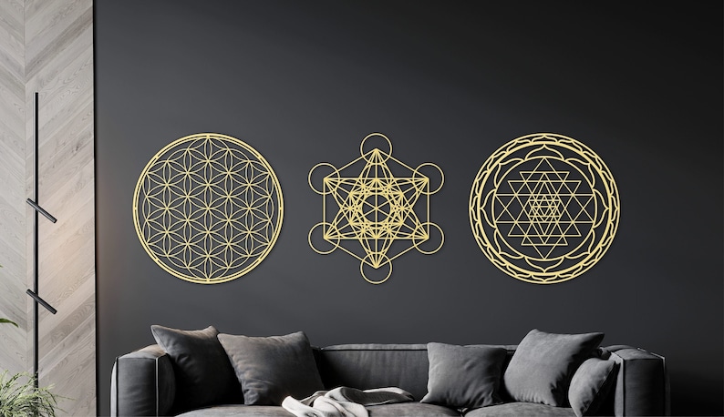 May include: Three gold metal wall decor pieces featuring geometric designs. The designs are a flower of life, a metatron's cube, and a sri yantra.