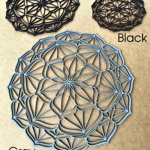 Op de afbeelding: Twee decoratieve wandhangers, een in zwart en een in grijs, met een geometrisch mandala-ontwerp. De grijze mandala is groter dan de zwarte mandala.
