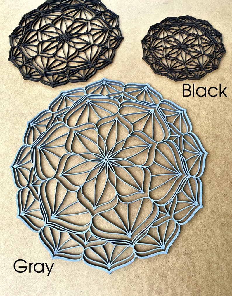 Op de afbeelding: Twee decoratieve wandhangers, een in zwart en een in grijs, met een geometrisch mandala-ontwerp. De grijze mandala is groter dan de zwarte mandala.