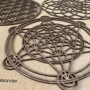 May include: Three wooden geometric wall art pieces in the shape of a flower of life, a star of david, and a metatron's cube. The pieces are made of palisander wood and have a dark brown color.