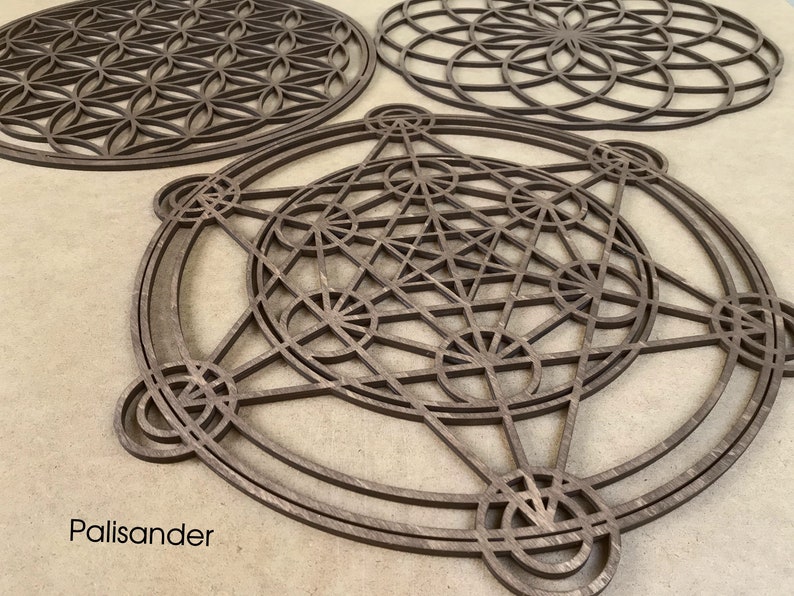 May include: Three wooden geometric wall art pieces in the shape of a flower of life, a star of david, and a metatron's cube. The pieces are made of palisander wood and have a dark brown color.