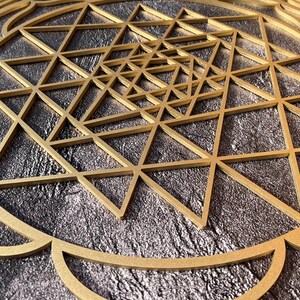 May include: A gold geometric design with a circular frame on a dark gray background. The design is made up of overlapping triangles.